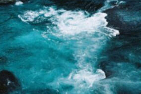 image ID: aquamarine water with white foam stretching from the mid top to mid bottom. the bottom left and top right are black